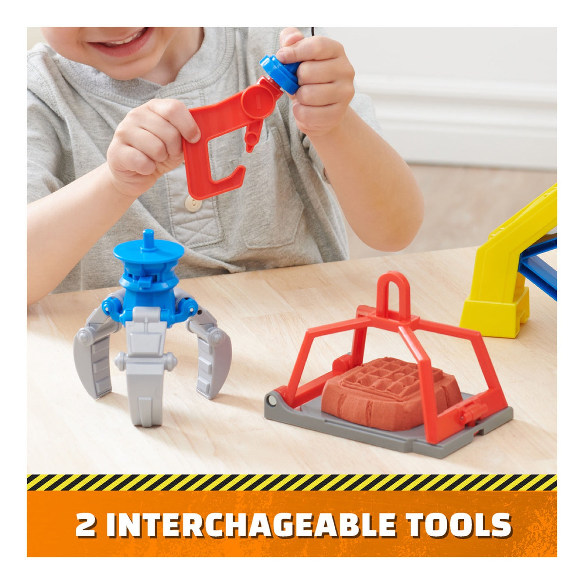Child swapping the crane grabber and hook tools beside a moulded sand block