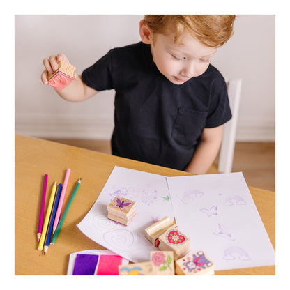 Child holding a wooden stamp above friendship drawings and colouring pencils