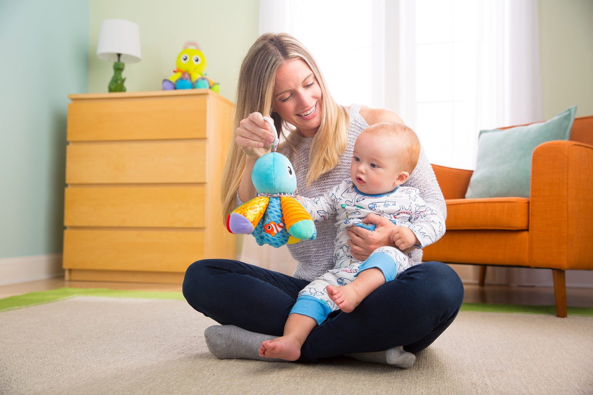 Parent holding Salty Sam clip-on octopus toy while seated with baby